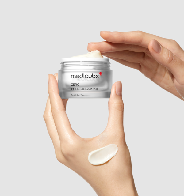 AgelessBeauty3000.com  medicube | Zero Pore Cream 2.0  Hand holding a jar of Medicube Zero Pore Cream 2.0 with a small amount on the palm against a light gray background.