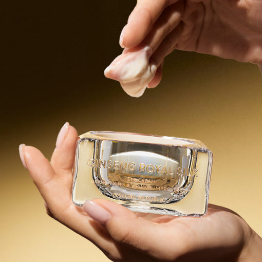 AgelessBeauty3000.com  NATURE REPUBLIC | Ginseng Royal Silk Eye Cream     Crimson Peak Ginseng Royal Silk eye cream in clear packaging held by a hand against a gold background