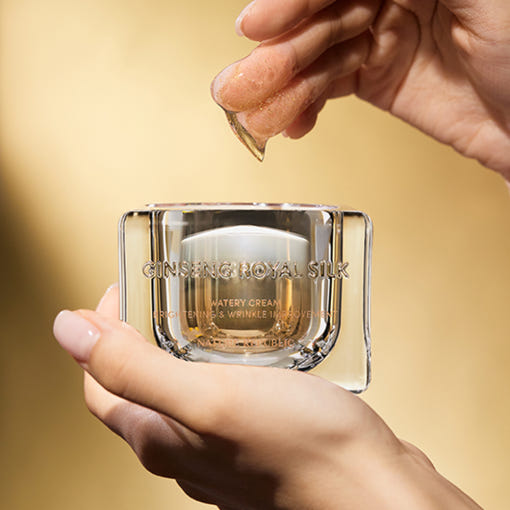 AgelessBeauty3000.com  NATURE REPUBLIC | Ginseng Royal Silk Watery Cream  Hand holding a glass container with Ginseng Royal Silk cream against a gold background