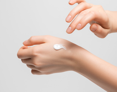 AgelessBeauty3000.com  Hand applying cream to another hand on a light gray background