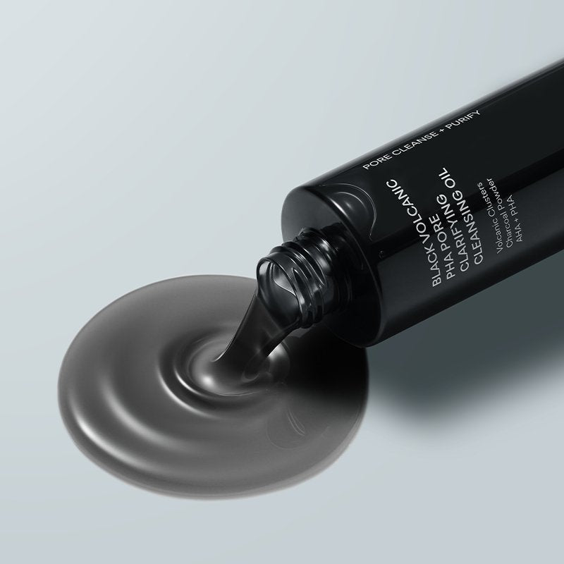 thatkbeautyshop.com   A black bottle of Black Volcanic Cleansing Oil with dark gel being poured onto a light gray surface, creating a circular pool of the product.