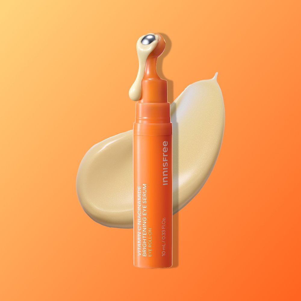 ThatKBeautyShop.com      Innisfree Vitamin C Niacinamide Brightening Eye Serum   Innisfree Brightening Eye Serum in an orange squeeze tube with a cream-colored rollerball applicator, set against a vibrant orange background with a beige cream smear behind it.